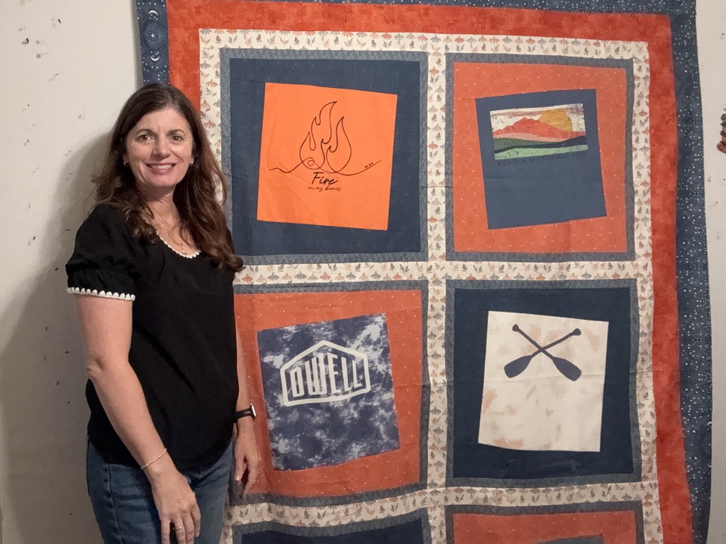Katie standing beside a finished wonky t-shirt quilt